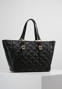 Black leather handbag with quilted diamond pattern, two handles with gold buckles, displayed on white surface against plain background.