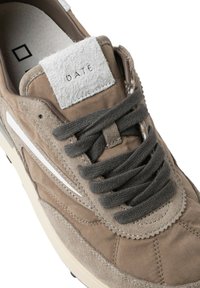 Baskets en daim marron avec une bande blanche sur le côté, une languette texturée ornée d'une étiquette en tissu portant la mention "DATE", et des lacets gris.