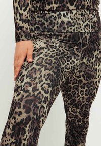 Leggings med leopardmönster i mjukt, stretcht tyg. Har hög midja och en slät yta med svarta och bruna fläckar på en tanfärgad bakgrund.