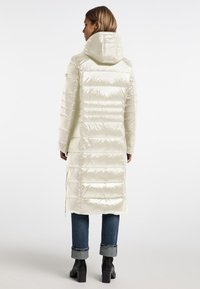 Lichtgekleurde, doorgestikte lange jas met capuchon, met een glanzende textuur en verticale stiksels. Gecombineerd met opgerolde denim en zwarte laarzen met hak.