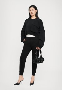 Black cropped sweatshirt with a front pocket, paired with black tapered sweatpants. Model holds a black handbag with studded details.
