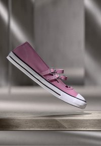 Shoe em tela cor de rosa, com duas tiras e detalhes de fivela prateada, apresentando uma biqueira em borracha branca e acabamento preto ao longo da sola.