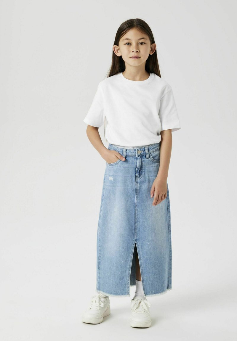 Maxi-Jeansrock mit Schlitz vorne, getragen über einem weißen Rundhals-T-Shirt. Das Outfit wird mit weißen Sneakers kombiniert.