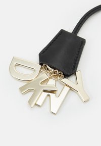 Musta nahkainen avaimenperä, jossa on kultainen metalliosio. Siinä on kultaiset isot kirjaimet "D", "A", "Y" lihavoidulla fontilla.