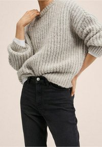 Suéter grueso de punto en gris claro con cuello redondo y textura acanalada, combinado con jeans negros de tiro alto con cierre de botón.