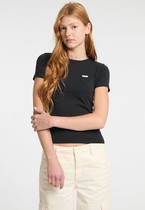 Schwarzes kurzärmliges T-Shirt mit rundem Ausschnitt und einem kleinen Brusttaschen-Detail, kombiniert mit beigen Cargo-Hosen.