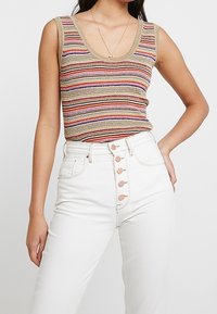 Stickad linne med flerfärgade ränder, guldkant och djup u-ringning, parat med högmidjade vita jeans med knapprad.