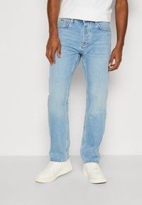 Vaqueros de denim azul claro con un diseño de pierna recta, estilo de cinco bolsillos y un ligero desgastado. Combinados con zapatillas blancas.