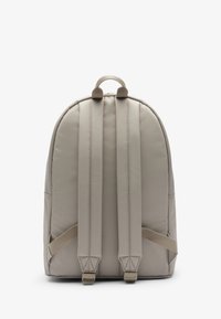 Beżowy plecak z wyściełanymi ramiączkami i uchwytem na górze, przedstawiony od tyłu na jednolitym białym tle.