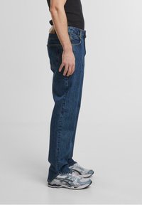 Jeans din denim albastru cu croială dreaptă, având un design cu cinci buzunare și cusături în contrast, asortați cu adidași gri deschis.