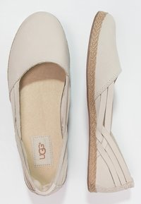 Zapatos planos beige sin cordones con una suela media de cuerda trenzada, cintas elásticas laterales y una plantilla suave con textura, mostrados desde vistas superior y lateral.