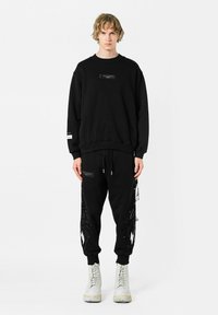 Sudadera negra y pantalones jogger con detalles gráficos, con un estampado texturizado en los pantalones y botas blancas en contraste.