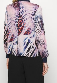 Long-sleeve blouse with a sheer, lightweight fabric featuring a colorful animal print in pink, red, blue, and black, with ribbed cuffs.
