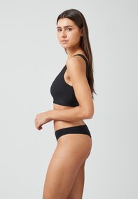 Czarny bawełniany bralet z grubymi ramiączkami i krojem crop, w zestawieniu z pasującymi, niskopodwieszanymi majtkami bikini, oba z minimalnymi szwami.