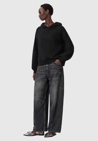 Felpa nera con cappuccio e maniche lunghe, abbinata a jeans di denim grigio scuro a gamba larga e scarpe basse nere e argentate a punta.