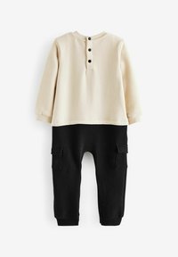 Top de manga larga beige con tres botones negros en la parte de atrás, combinado con pantalones de forro polar negros que cuentan con dos bolsillos laterales.