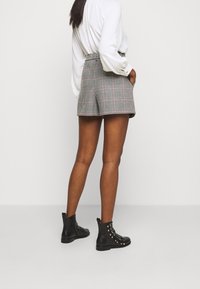 Zwart-witte geblokte shorts met een hoge taille, gecombineerd met een witte lange mouwen shirt en zwarte leren enkelschoenen met studs.