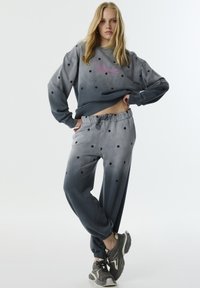 Grijze ombré sweater en broek set met zwarte stippen, voorzien van een ronde halslijn en een elastische tailleband. Gepaard met grijze sportschoenen.