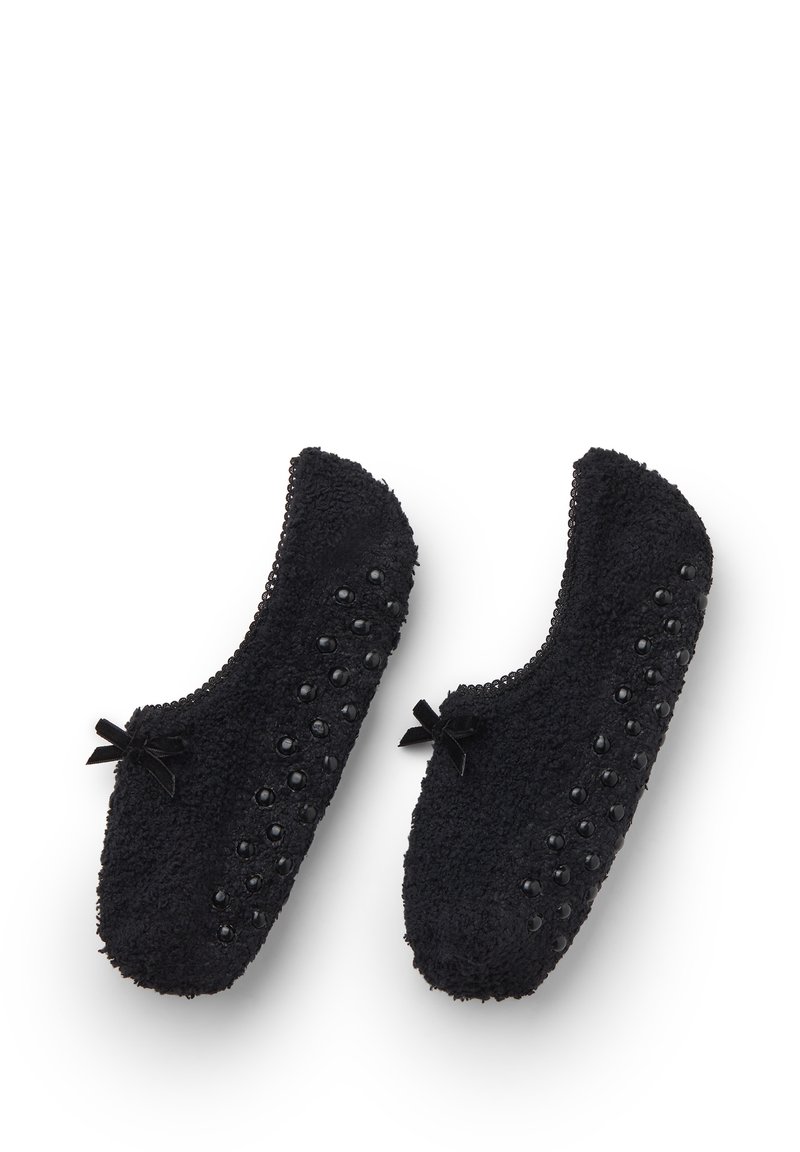 Coppia di pantofole da interno nere e pelose con punti in gomma antiscivolo sulla suola e piccoli fiocchi decorativi sulla parte superiore.