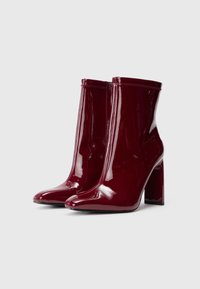 Botas de tornozelo em couro laca bordeaux com um acabamento brilhante, bico fino e salto bloco. Apresenta um fecho de correr e borda superior costurada.