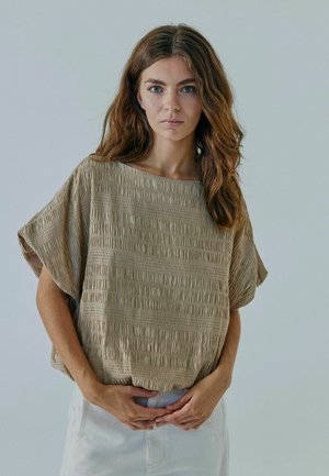 Beżowa, teksturowana bluzka z krótkim rękawem i luźnym krojem. Posiada pionowe i poziome żłobienia, połączona z jasnym dołem.