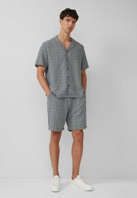 Korte mouwen overhemd en shorts set in een geruite grijze stof met blauwe en rode accenten, voorzien van een knoopsluiting aan de voorkant en zijzakken.