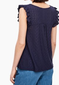 Haut bleu marine en tissu œillet avec un motif texturé et des manches volantées. Coupe décontractée et encolure arrondie, assorti à un jean en denim.