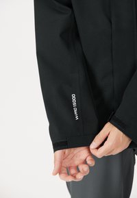 Sort jakke med et elegant design, der har WP 15000 branding på manchetten og velcro lukning ved håndleddet. Glat stoftekstur.