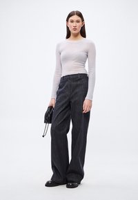 Svetlo siva dolg rokav s rebrasto tkanino, kombiniran s temnimi širokimi hlačami. Model drži majhno črno torbico; čevlji so črni z okroglo toe.