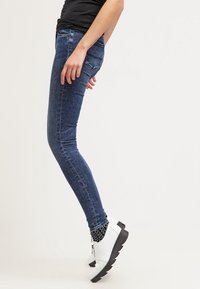 Vaqueros skinny de mezclilla en azul oscuro, con diseño de cinco bolsillos y una silueta ajustada, combinados con botas blancas hasta el tobillo y calcetines con estampado.