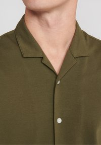 Olivgrön skjorta med krage i mjukt tyg, med knappstängning och en minimalistisk design. Korta ärmar och rena linjer.