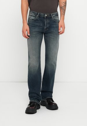 Donkerblauwe spijkerbroeken van denim met een vervaagde textuur, rechte pijpen, vijf zakken en een metalen knoopsluiting, gecombineerd met zwarte dikke schoenen.
