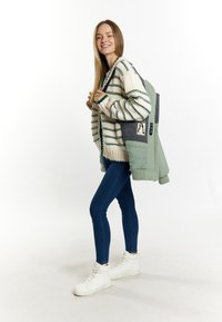 Gebreide trui met groene strepen, lichtgroene pufferjack, blauwe jeans en witte hoge sneakers. Rugzak heeft een grafische patch.