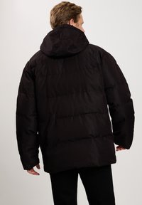 Czarna kurtka puchowa z kapturem, poziomymi szwami i luźnym krojem. Materiał wydaje się miękki o gładkim, matowym wykończeniu.