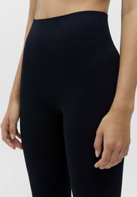 Leggings noires à taille haute, côtelés, avec une texture lisse, un design près du corps et des bords sans couture, adaptées à diverses activités.