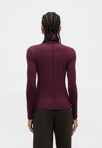 Μπλούζα με μακριά μανίκια και ζιβάγκο σε βαθύ μωβ χρώμα, με εφαρμοστή σχεδίαση, κεντρική ραφή και απαλή υφή υφάσματος.