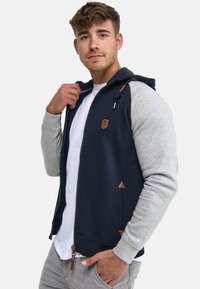 Navy and gray zip-up hoodie made of cotton blend, featuring leather accents, triangular details, and a drawstring hood.