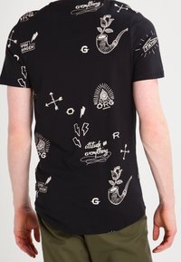 Camiseta negra con diseños gráficos blancos que incluyen tuberías con rosas, flechas, rayos y texto como "la actitud lo es todo" y "Copenhague."