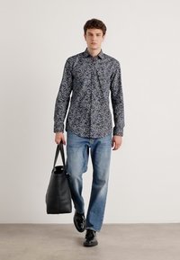 Long-sleeved, navy patterned shirt, light blue jeans, black leather shoes, and a black tote bag. Casual fit, smooth fabric, and button-up design.