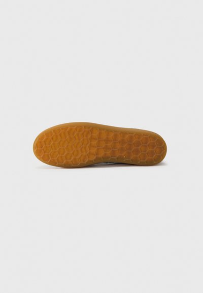 Semelle de chaussure avec motif de semelle alvéolaire en caoutchouc brun translucide sur fond blanc uni.