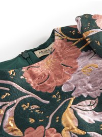 Virágmintás ruha sötétzöld anyagból, rózsaszín és arany hímzett virágokkal. Figyelemre méltó részletek közé tartozik a kerek nyakkivágás és a láthatatlan cipzár.