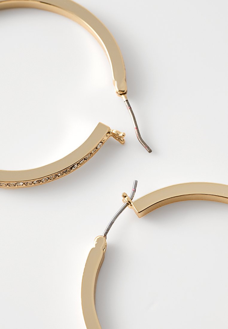 Pendientes de aro de metal tono dorado con un acabado liso, una pequeña sección adornada con rhinestones y un cierre de bisagra.