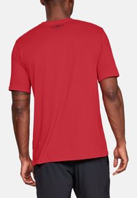 T-shirt rouge à manches courtes avec un col rond, texture lisse et un petit logo noir au dos. Design simple, coupe décontractée.