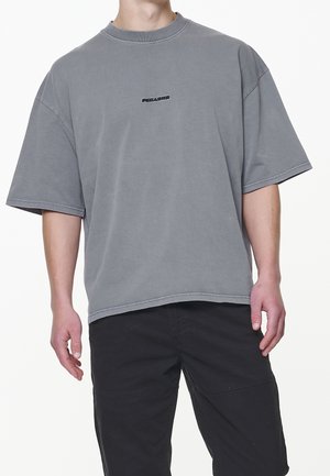 Graues übergroßes T-Shirt mit rundem Ausschnitt und kurzen Ärmeln. Verfügt über ein kleines schwarzes Logo auf der Brust und sichtbare Nähte.