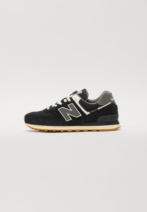Baskets New Balance noires et grises avec lacets blancs, semelle beige et étiquette en tissu « Cordura » sur le côté, vues de profil.