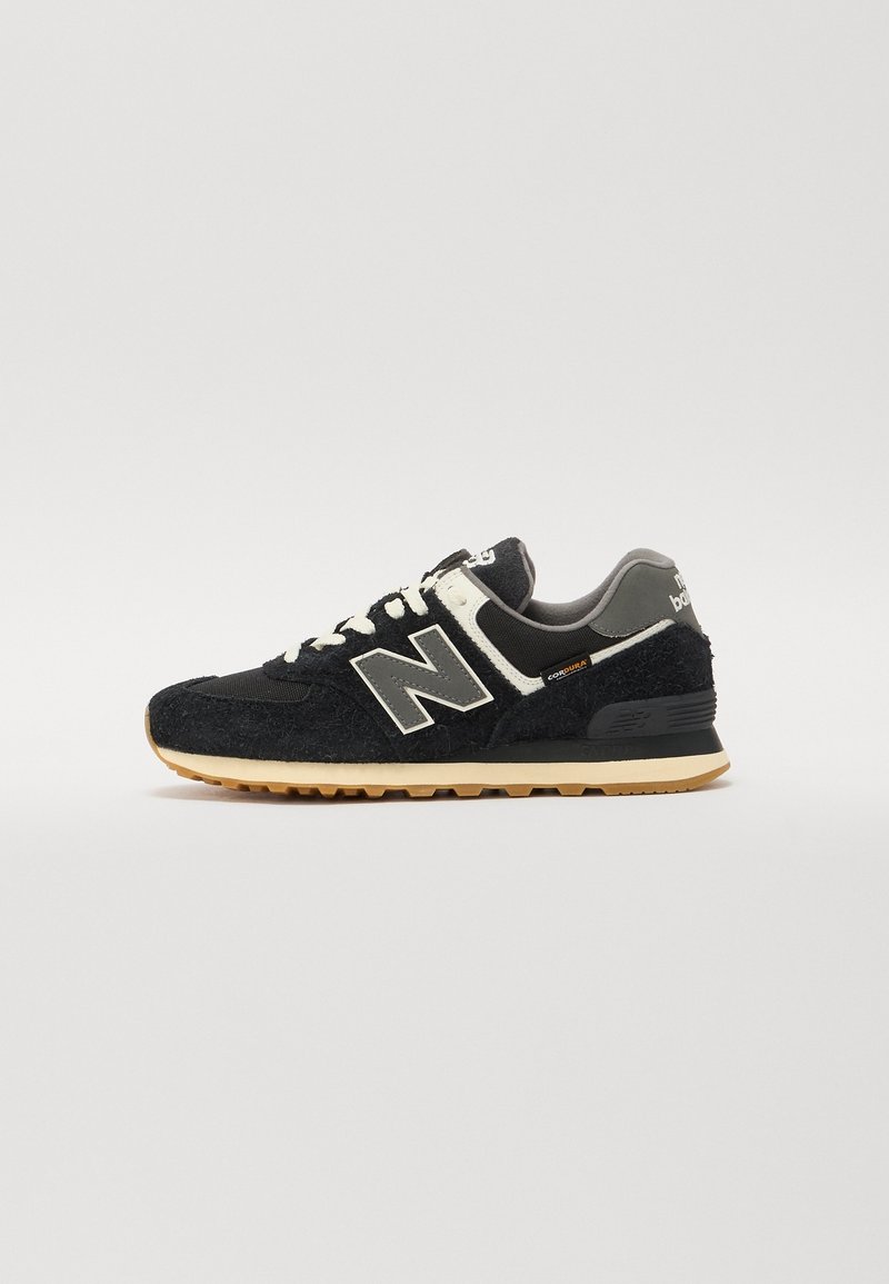 Baskets New Balance noires et grises avec lacets blancs, semelle beige et étiquette en tissu « Cordura » sur le côté, vues de profil.