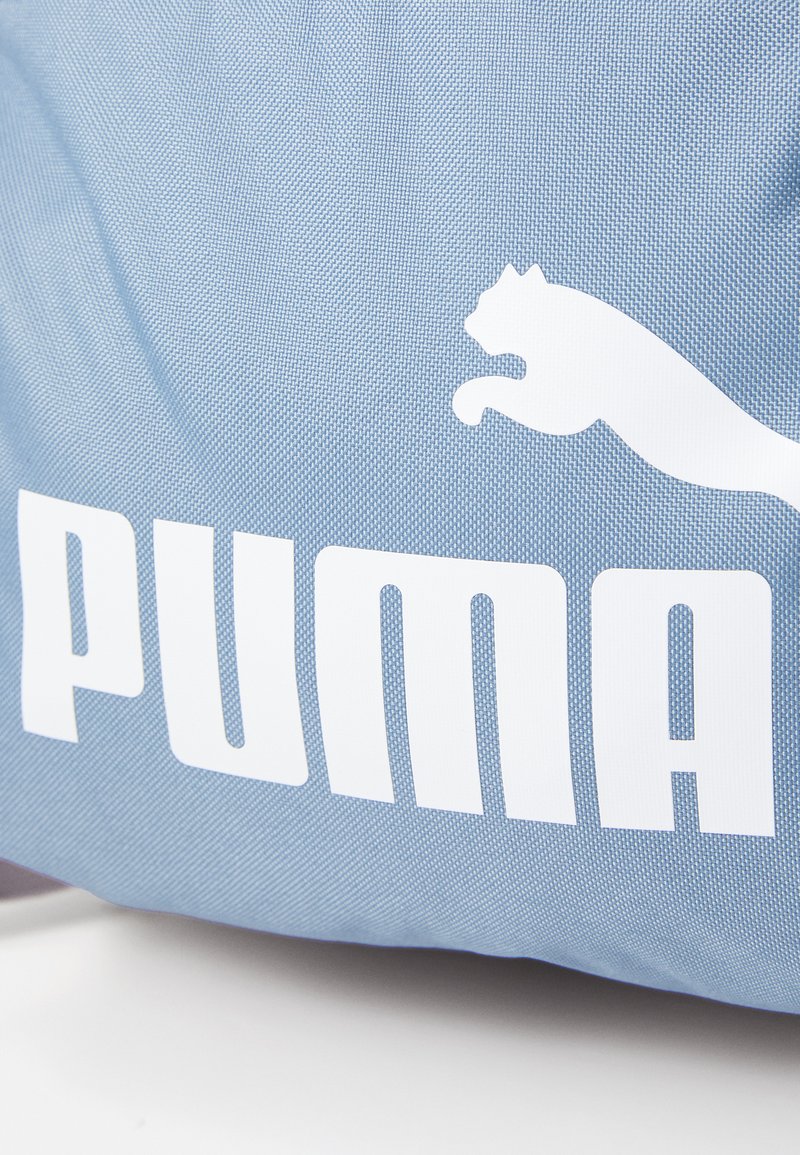 Bolsa de tela sintética de color azul claro con una superficie texturizada, que presenta un prominente logo en blanco de "PUMA" y un diseño de un gato saltando.