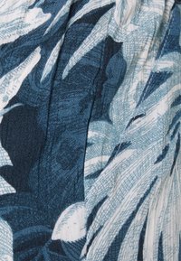 Skládaná látka s modro-bílým tropickým listovým vzorem. Materiál má texturovaný vzhled, což zvyšuje hloubku a detaily.