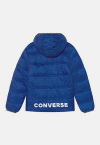 Blå puffjacka med huva, med horisontella quiltade sektioner och en stor vit "CONVERSE"-logotyp på baksidan.