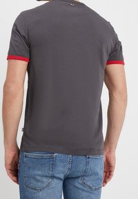 Tummanharmaa lyhythihainen T-paita, jossa punainen yksityiskohta hihoissa, pyöreä kaulus ja pieni logotunnus lähellä kaulusta.